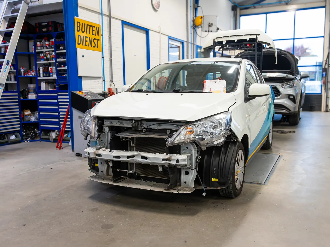 Een witte auto zonder bumper en koplampen in de werkplaats, klaar voor herstel van de voorkant.