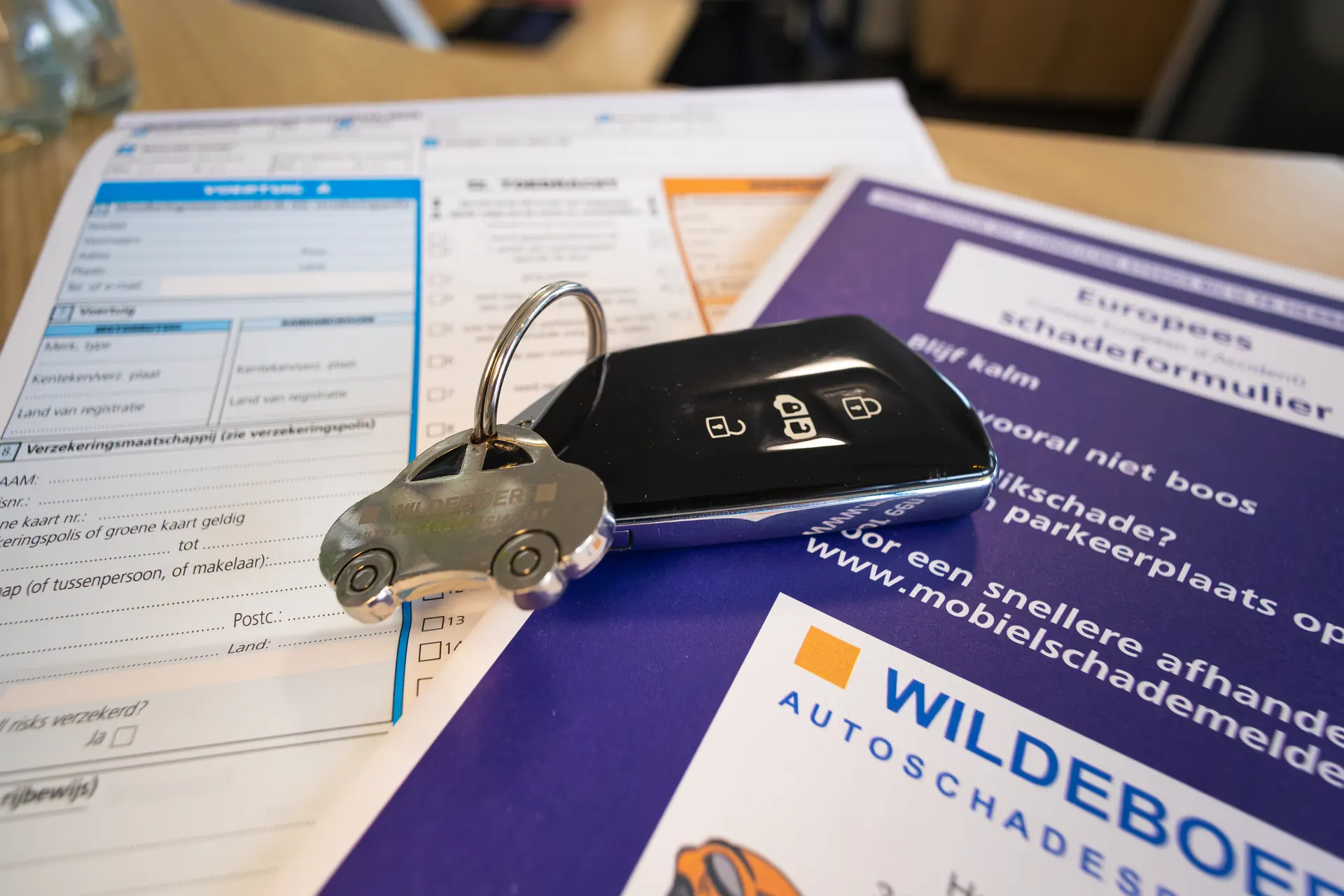 Een Europees schadeformulier op tafel met een autosleutel met een Wildeboer-sleutelhanger erop.