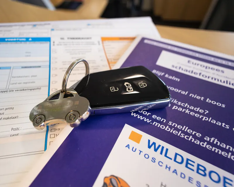 Een Europees schadeformulier met een autosleutel met een Wildeboer-sleutelhanger.