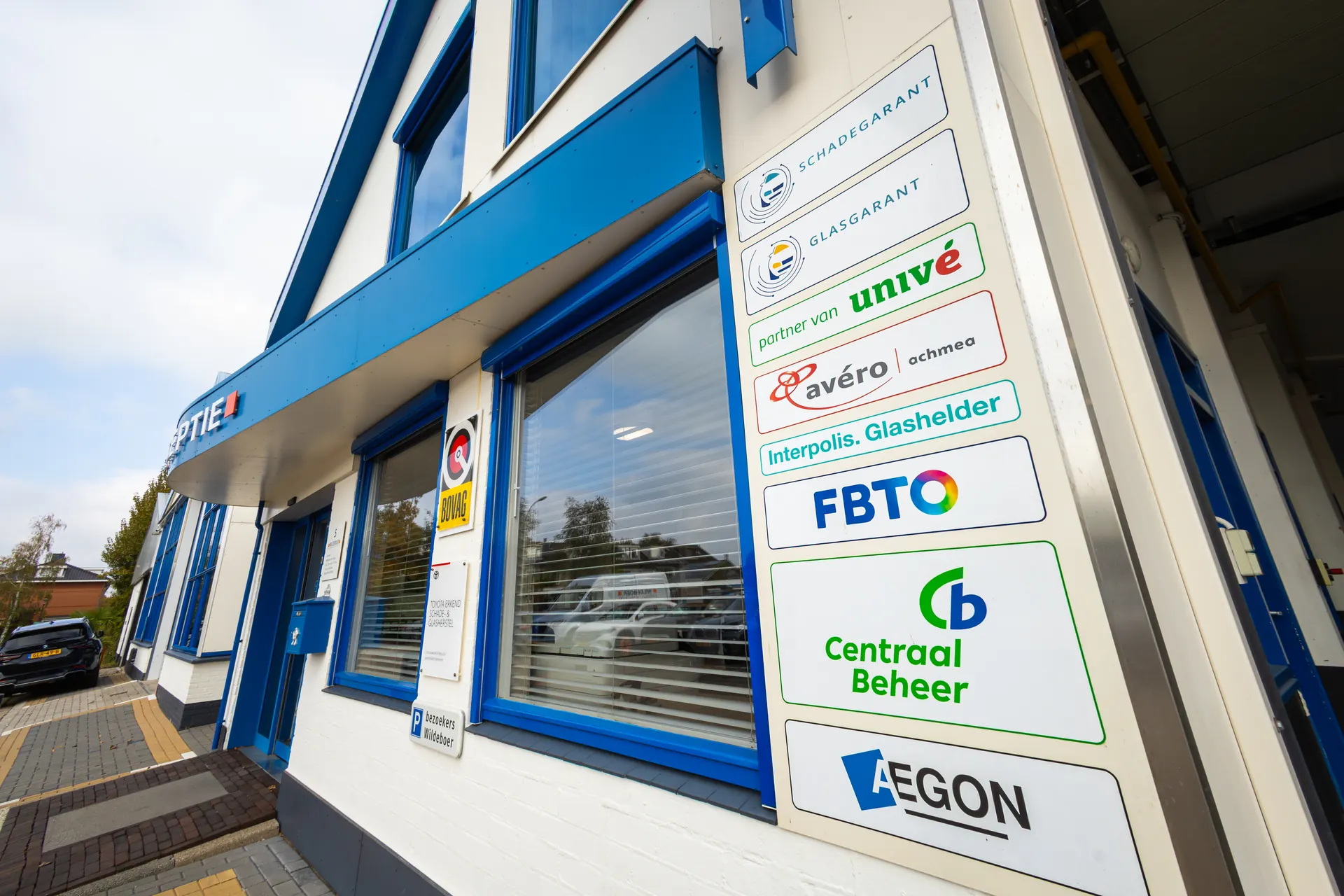 De bordjes van de verzekeraars naast de ingang van Wildeboer: Schadegarant, Glasgarant, Univé, Avéro Achmea, Interpolis Glashelder, FBTO, Centraal Beheer en Aegon.
