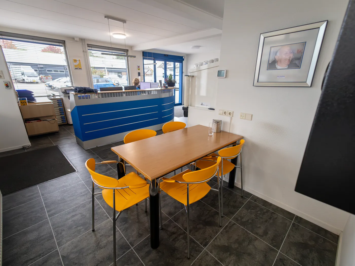 De wachtruimte van Wildeboer met een tafel, oranje stoelen en de koffieautomaat.
